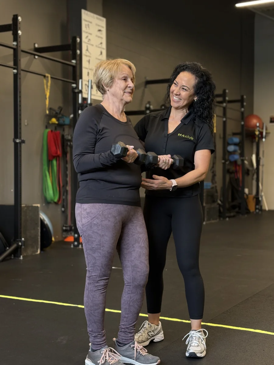 Elderly woman lifts dumbbells with a female trainer overseeing her