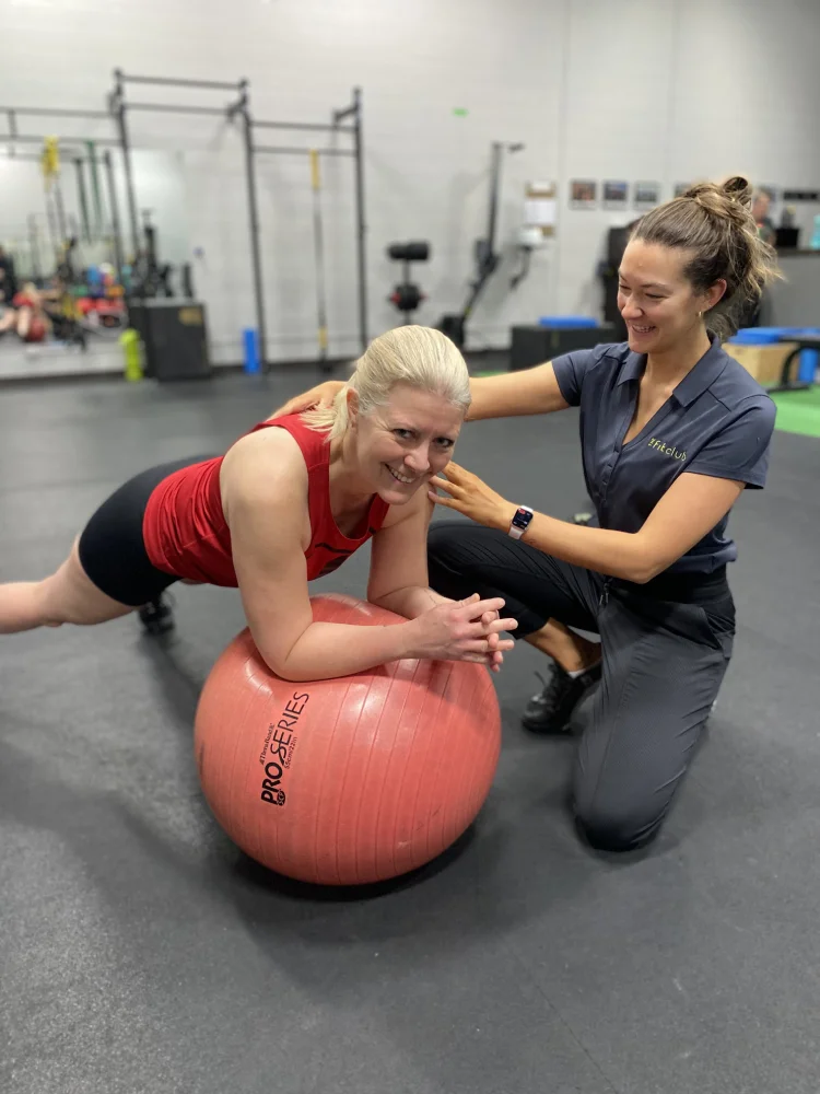 Female trainer oversees woman doing plank exercise on medicine ball